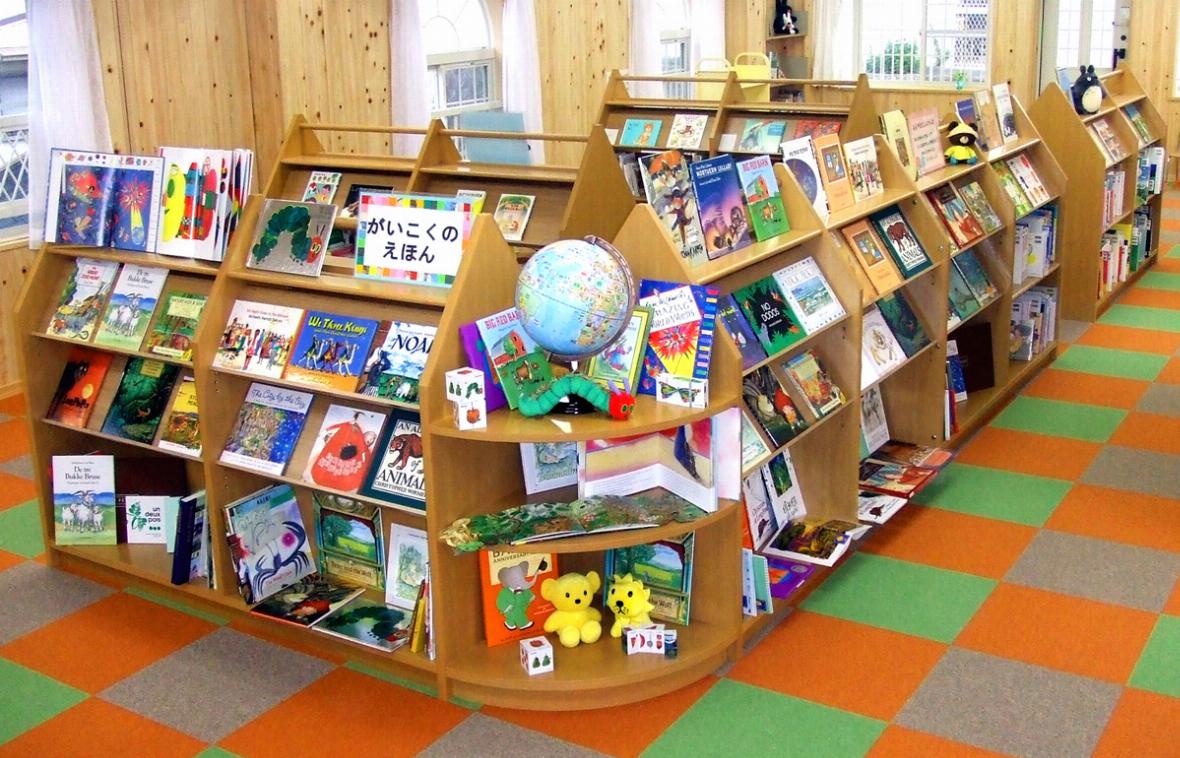 たくさんの絵本が並ぶ、木製の書棚と明るい日差しが差し込む絵本館
