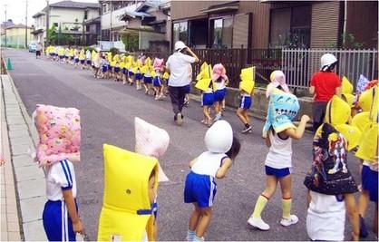 避難訓練で、防災頭巾を被り、列になって公道を歩く先生と園児達